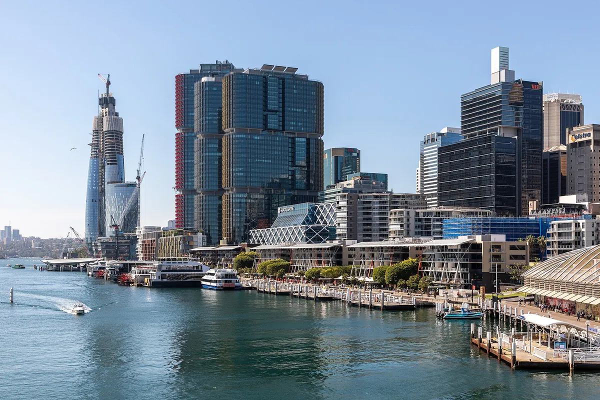 The Darling Harbour waterfront by day, with cruise boats moored along the wharves in front of the city towers and a harbour ferry wharf at the right.